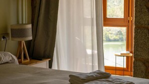 Ein Hotelzimmer mit Bett, Lampe, einem Fenster mit Vorhängen und Blick auf eine Landschaft.