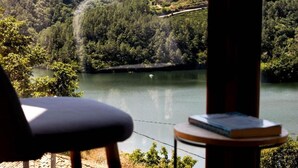 Blick auf einen See mit einem Stuhl und einem Tisch mit einem Buch, umgeben von bewaldeten Hügeln.