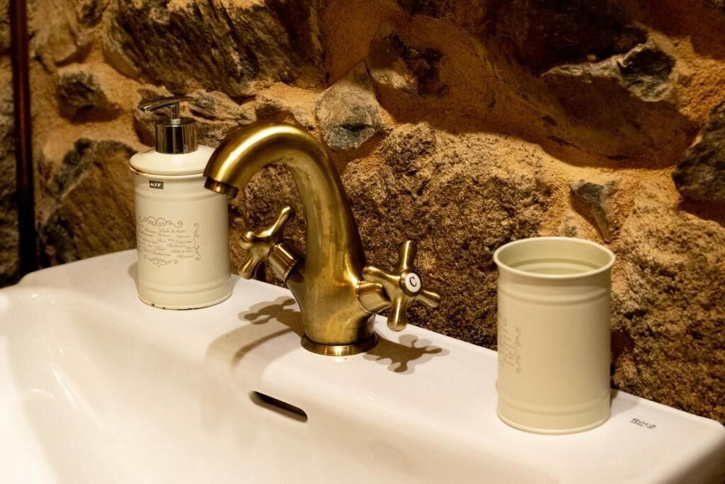 Een wastafel met een messing kraan, een witte fles en een wit kopje.