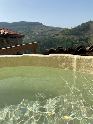 A clear pool with a wooden bench, surrounded by terracotta roof tiles and a stone wall.