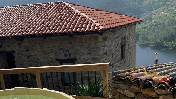 Ein Steinhaus mit rotem Ziegeldach, einer Holzterrasse und einem Whirlpool.