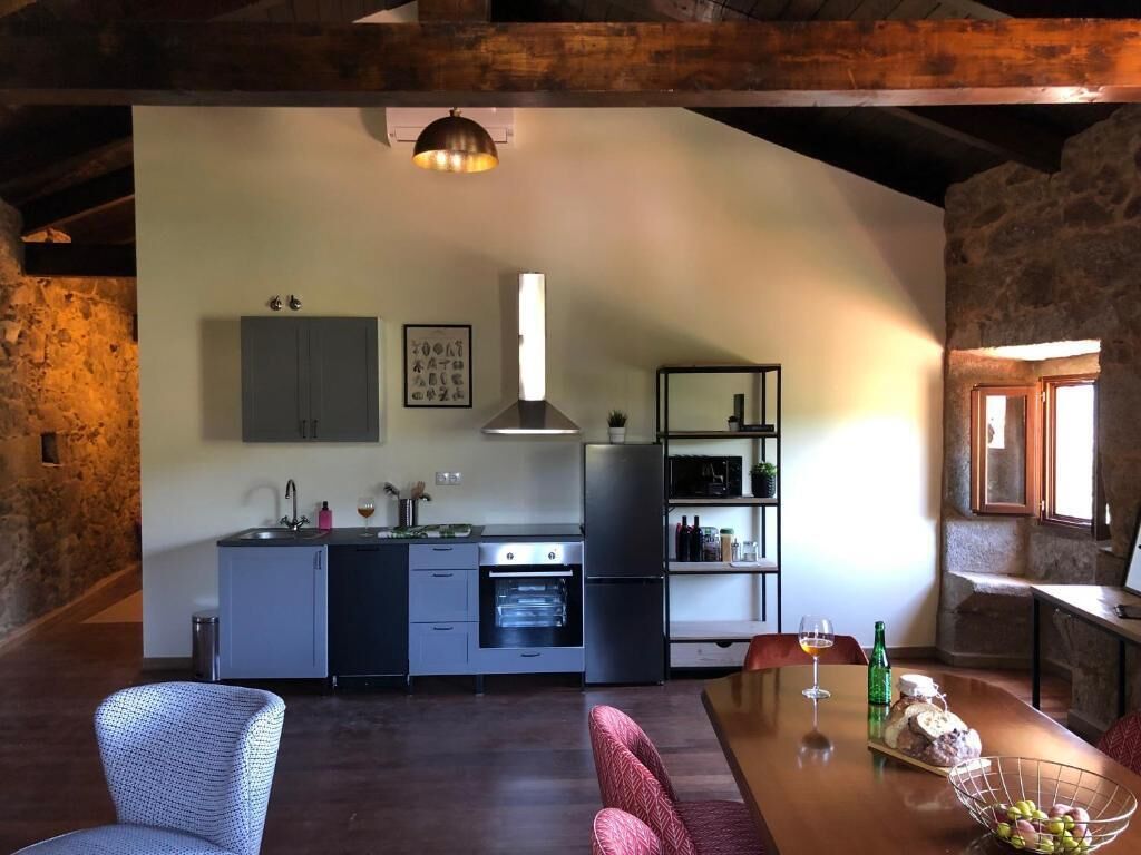 Una cocina moderna con comedor, que cuenta con una pared de piedra, vigas de madera y un ventanal grande.