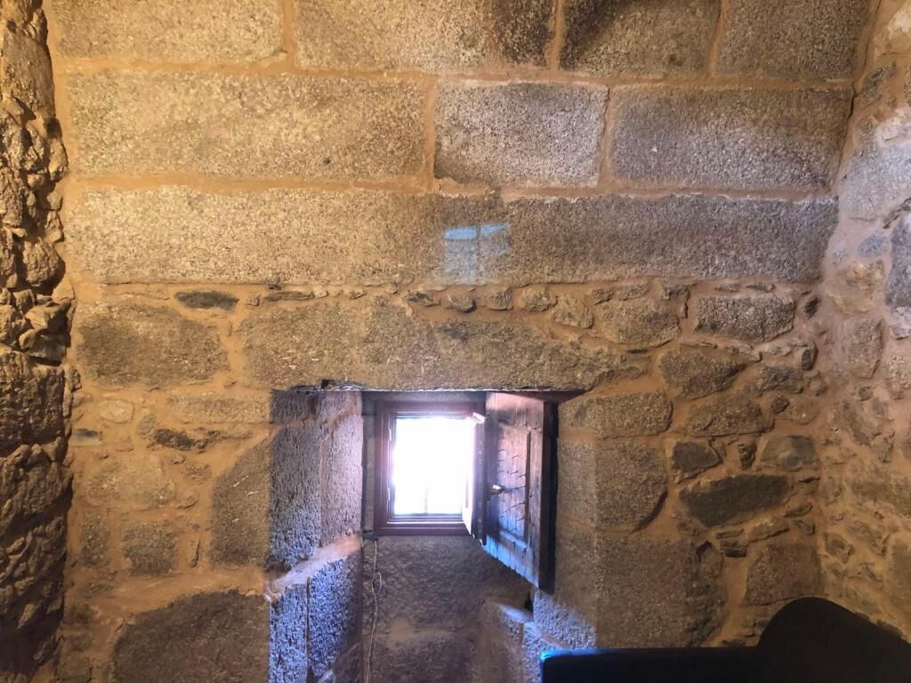 Un étroit couloir en pierre, avec une petite fenêtre au bout.