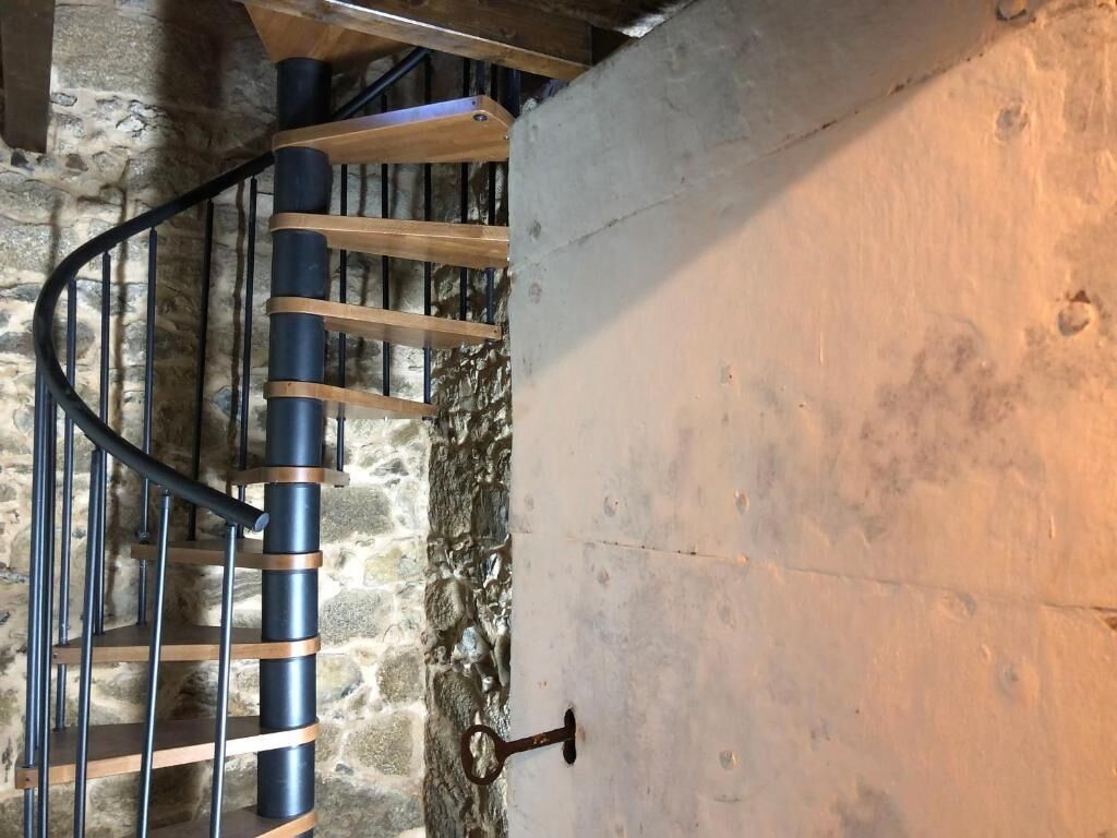 A spiral staircase with wooden steps and metal railings, leading to a stone wall.
