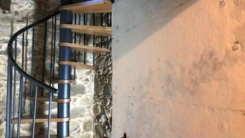 A spiral staircase with wooden steps and metal railings, leading to a stone wall.