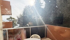 Ein Balkon mit rundem Tisch und weißen Plastikstühlen, mit Blick auf Bäume und ein Gebäude.