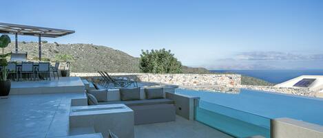 A modern outdoor lounge area with a pool, seating, and a view of the sea.