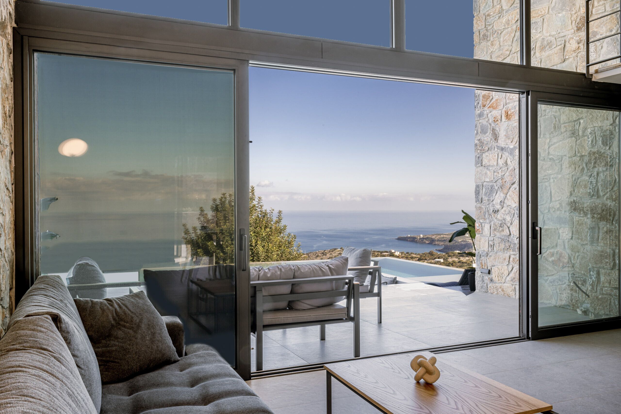 Una sala de estar moderna con un gran ventanal que da a una piscina y vista al océano.