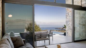 Una sala de estar moderna con un gran ventanal que da a una piscina y vista al océano.