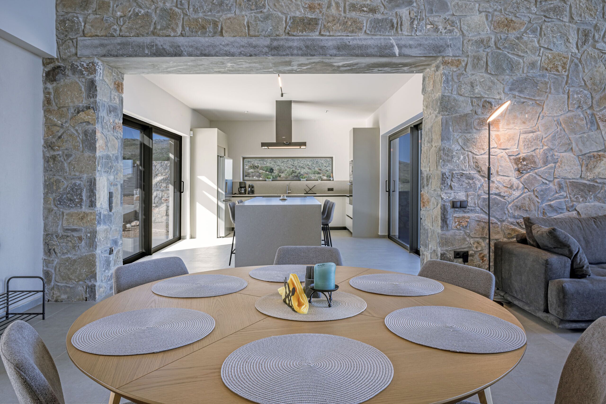 Un comedor moderno con un arco de piedra, una mesa redonda de madera con posavasos y vistas de la cocina y el comedor al fondo.