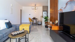 A modern living room with a sofa, coffee table, and a TV. There is a dining area with a table and chairs. - Flair 1-BR Apt. & Balcony in Larnaca (Larnaca)