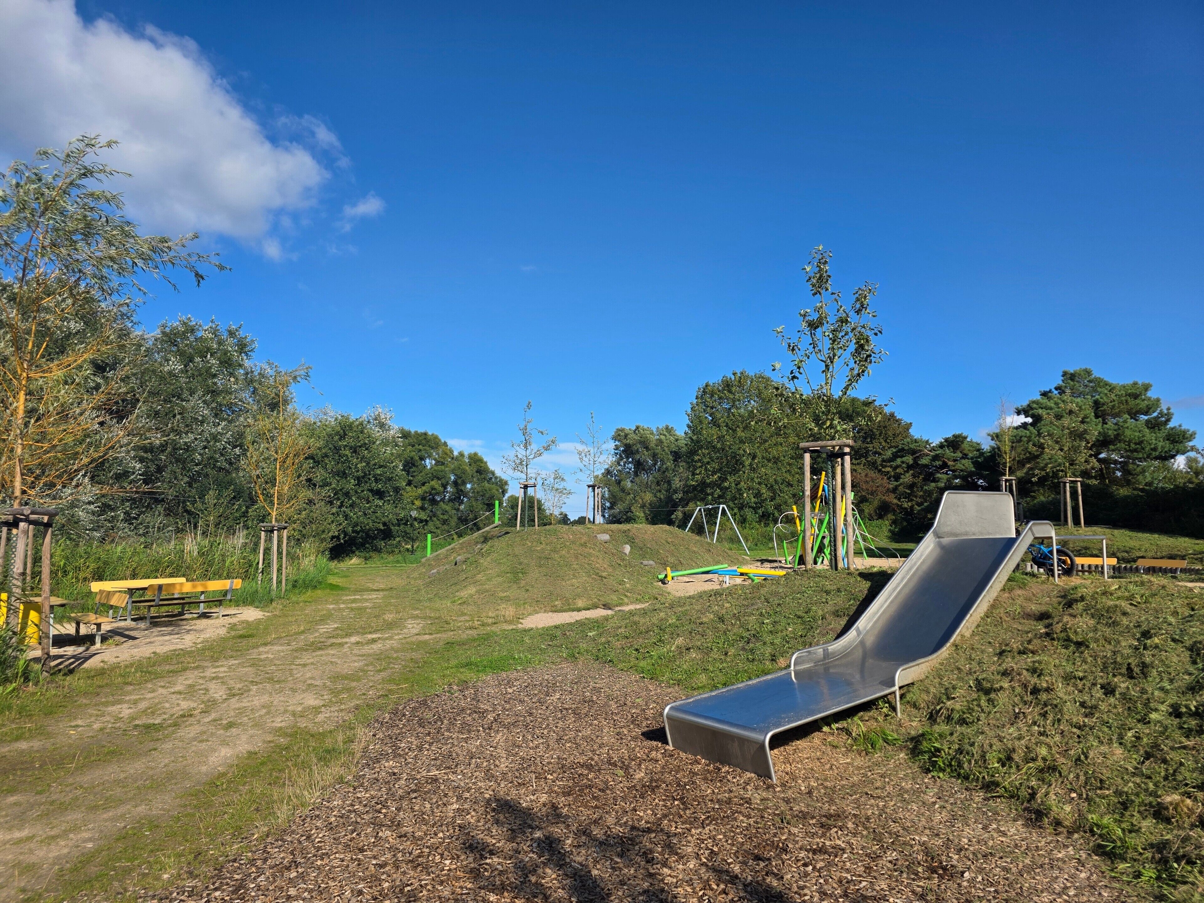 Une aire de jeux avec un toboggan, des bancs et des arbres.
