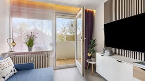 Una sala de estar moderna con un sofá, un televisor, una mesita con una planta y un ventanal corredizo al exterior.