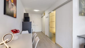 Una habitación de hotel moderna con un escritorio blanco, sillas, un jarrón de flores, un reloj y una puerta con pomo dorado.