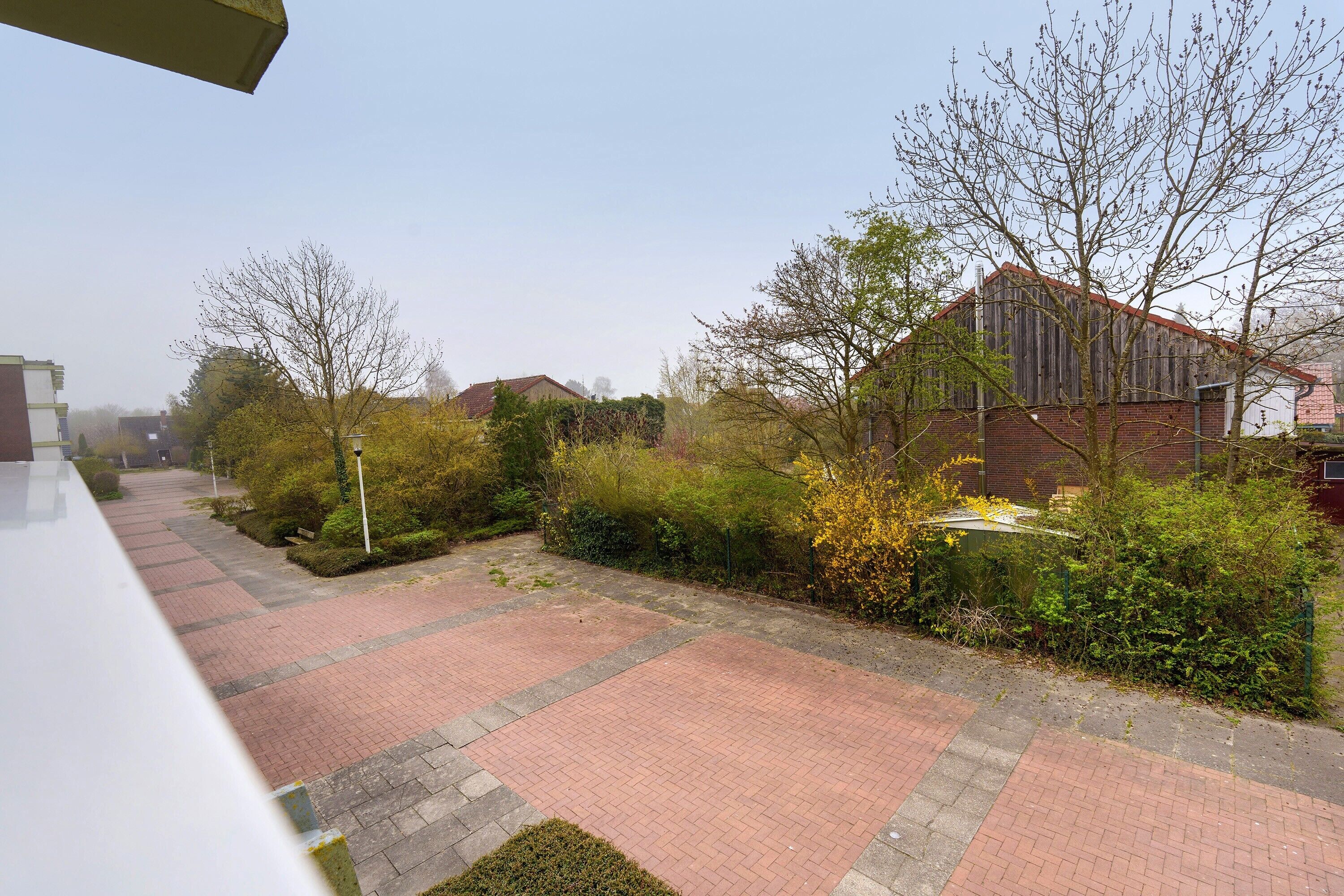 A paved courtyard with brick pathways, a brick building, and surrounding greenery.