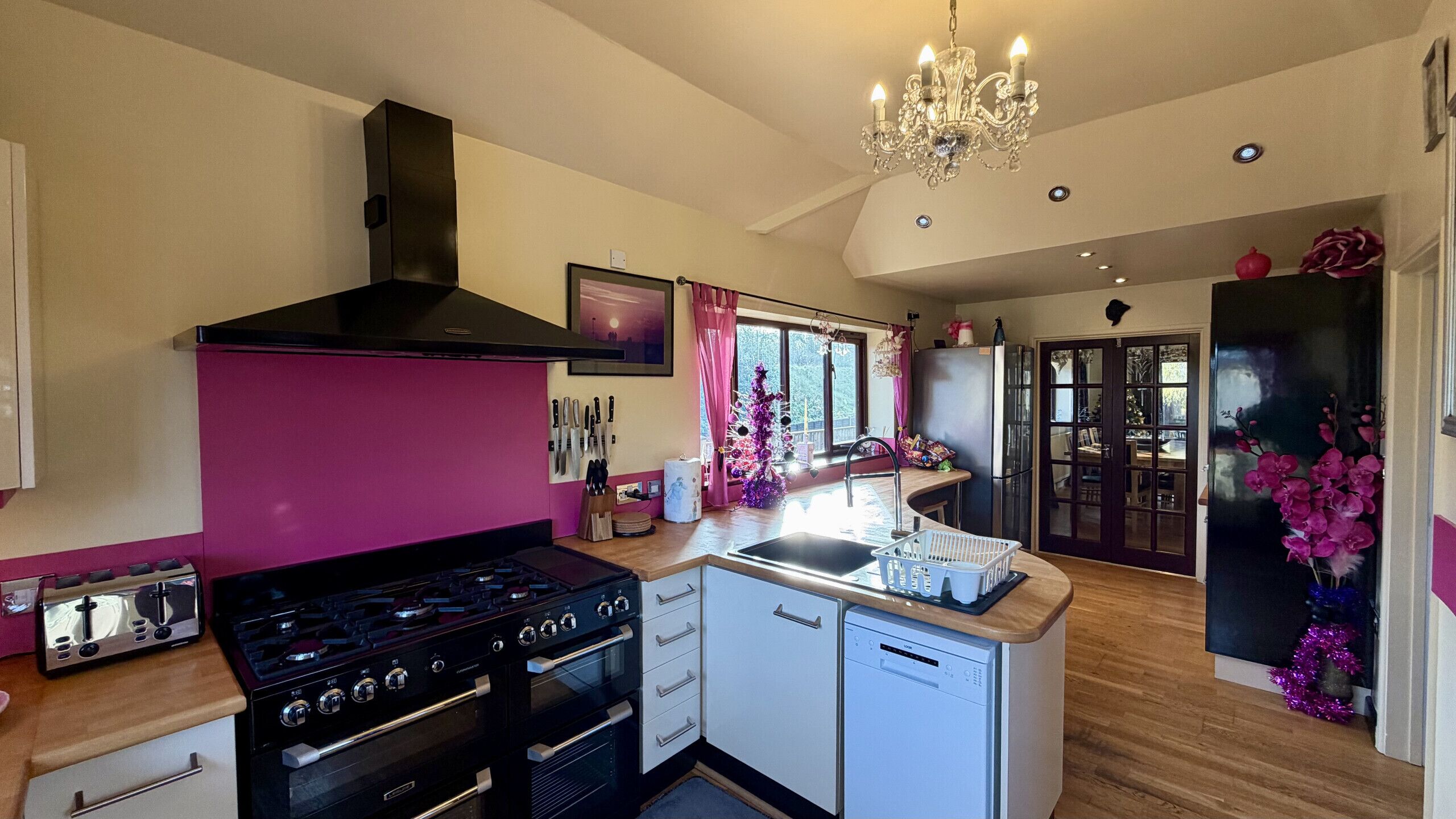 A compact kitchen with a gas stove, oven, and dishwasher, a black range hood, and a pink accent wall.
