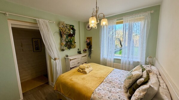Une chambre à coucher comprenant un lit, une commode, une fenêtre avec des rideaux, un lustre et une horloge murale.