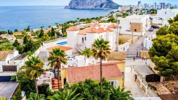 A coastal town with white buildings, palm trees, and a rocky island in the background. - Casa Armonia - Turquesa Charming 1-room studio with terrace and pool view (Benisa)