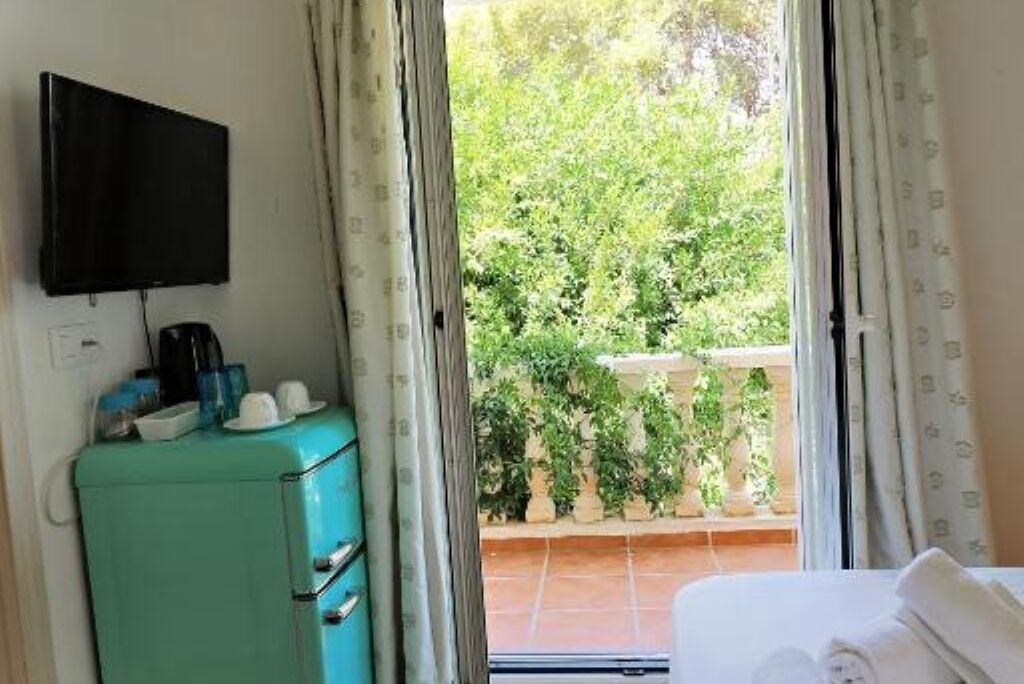 Habitación con cama, televisor montado en la pared, kitchenette con refrigerador y vistas a un balcón con plantas.
