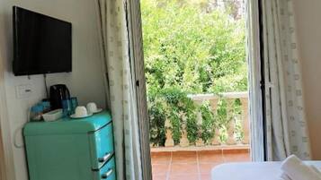 Habitación con cama, televisor montado en la pared, kitchenette con refrigerador y vistas a un balcón con plantas.