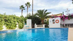 Una piscina con un muro blanco y un flotador salvavidas, rodeada de vegetación y palmeras.