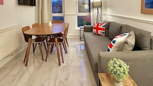 Un salon moderne avec un coin repas, un canapé orné de drapeaux britanniques et un téléviseur fixé au mur.