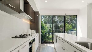 A modern kitchen with white cabinetry, a gas stove, and a large window overlooking a garden. - Modern 3BR House, 7min Drive to Leppington Station (Austral)