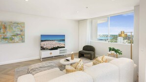 Een moderne woonkamer met een groot raam, een flatscreen televisie, een zithoek en een minimalistische witte console.