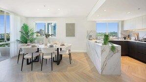 Een moderne keuken met een marmeren eiland, een eethoek met witte stoelen en grote ramen met uitzicht op de stad.