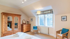 A bedroom with a large bed, wooden wardrobe, a chair, a dresser, and a window with a view of trees. - Beautiful private villa for 10 people with WIFI, TV, terrace and pets allowed (Newtonmore)