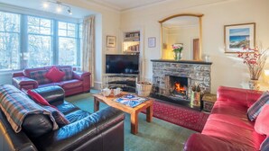 A cozy living room with a fireplace, leather sofas, a flat-screen TV, and a large window. - Beautiful private villa for 10 people with WIFI, TV, terrace and pets allowed (Newtonmore)
