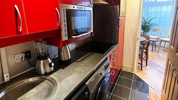 Une cuisine compacte avec des meubles rouges, un four à micro-ondes, une machine à café et un lave-vaisselle.