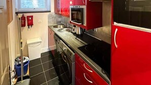 Une cuisine de taille réduite avec des meubles rouges, une cuisinière noire et une fenêtre donnant sur un beau paysage.