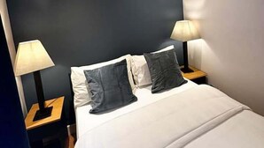 Une chambre d’hôtel moderne avec un grand lit, deux tables de chevet et un mur d’accent de couleur foncée.