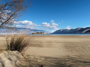 Een strand met een heldere lucht, bergen op de achtergrond en weinig begroeiing.