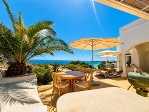 A patio with a table, chairs, and a grill, overlooking a coastal view.