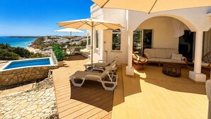 Un espace extérieur ensoleillé avec une piscine, des chaises longues et des parasols, offrant une vue imprenable sur la côte.