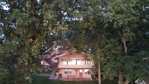 Une maison à deux étages, avec un chemin de pierres menant à la porte d’entrée, entourée d’arbres et d’un petit abri de jardin.