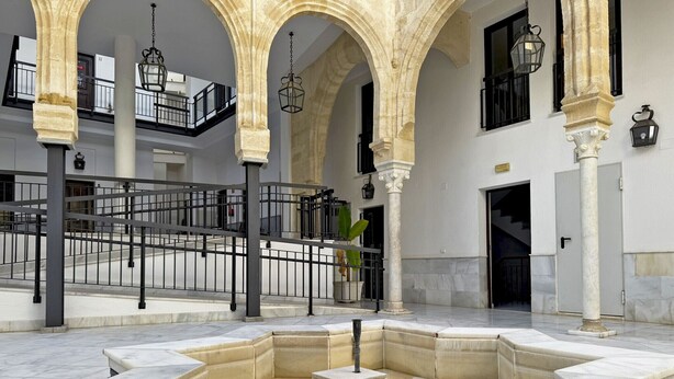 Un patio con una fuente, columnas de piedra y una escalera que lleva a un nivel superior.