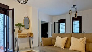 Un salón moderno con una mesa de centro de vidrio, un sofá color beige y una mesita de noche de madera con un espejo y una planta.