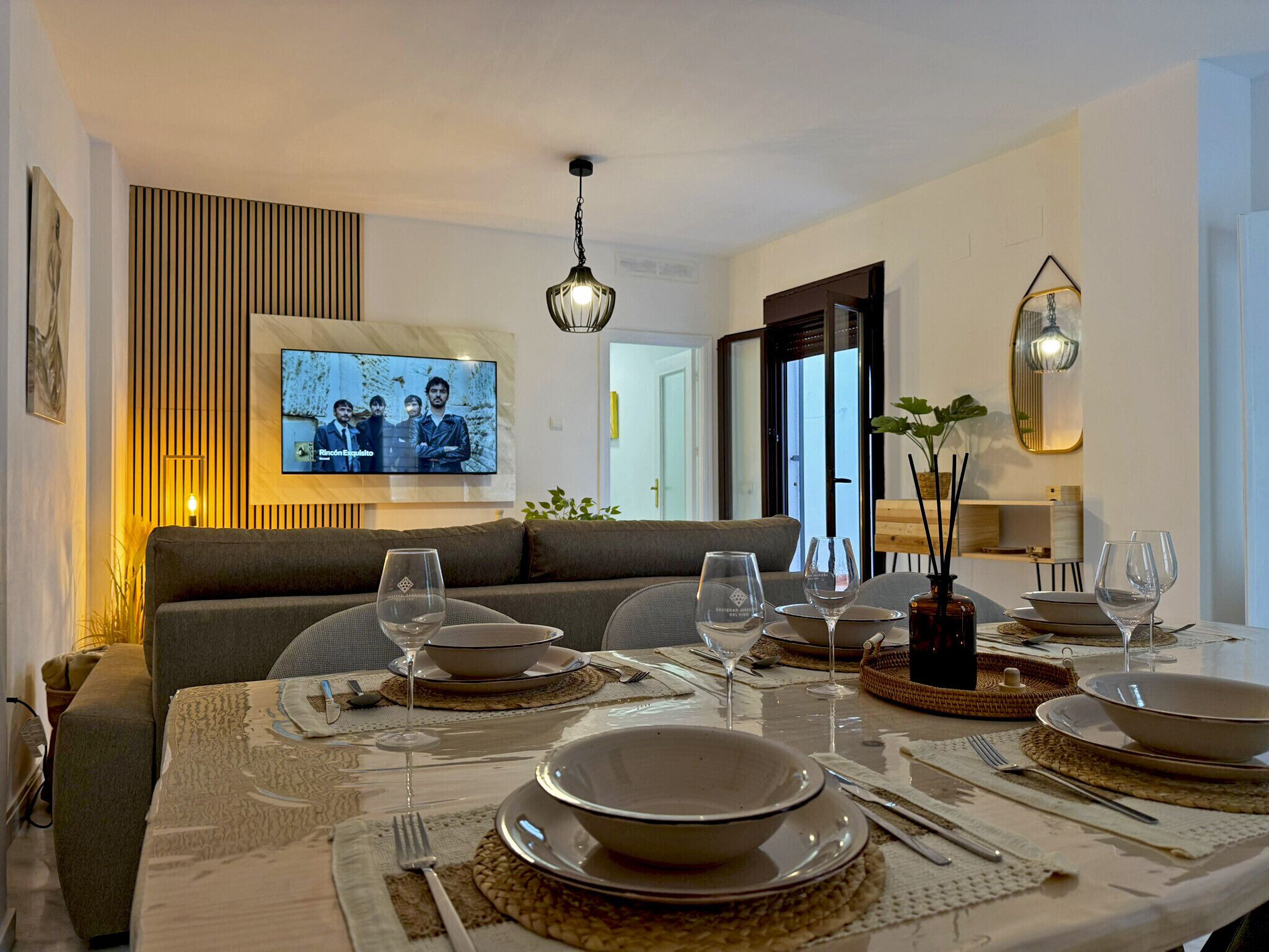 Een eethoek met een tafel voor vier personen, een aan de muur bevestigde televisie en een bank op de achtergrond.