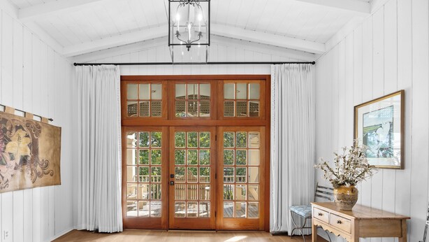 Ein Zimmer mit Holzböden, einer großen Holztür mit Glasfeldern, einem Schreibtisch mit einer Vase und einem Gemälde an der Wand.