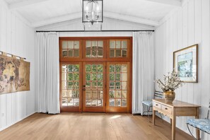Ein Zimmer mit Holzböden, einer großen Holztür mit Glasfeldern, einem Schreibtisch mit einer Vase und einem Gemälde an der Wand.