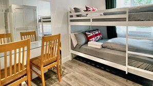 A compact room with bunk beds, a wooden dining table, chairs, and a small kitchenette. - Sunny Neasden Apartment (London)