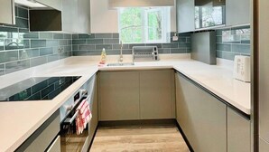 A modern kitchen with grey cabinets, a white countertop, and a window providing natural light. - Sunny Neasden Apartment (London)