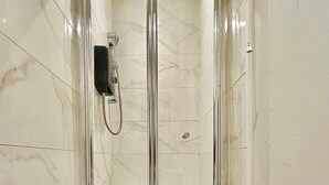 A glass-enclosed shower stall with a handheld showerhead, a small bottle of shampoo, and a single towel hanging on the wall. - Ground-floor Flat 1 Min to Tube (London)