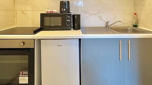 A compact kitchen with a built-in microwave, a small refrigerator, and a sink. - Ground-floor Flat 1 Min to Tube (London)