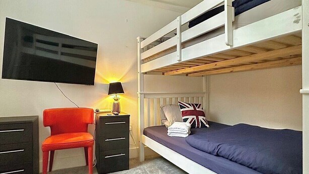 A bunk bed with a television above it, a desk with drawers, a chair, and a lamp. - Ground-floor Flat 1 Min to Tube (London)
