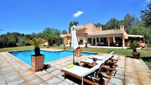 Area piscina con poltroncini, piscina e una casa sullo sfondo.