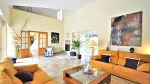 A spacious living room with a sofa, a coffee table, and a fireplace. There is a staircase leading to an upper level, and a large abstract painting on the wall. - Sa Rota | Pool, Tennis & Nature (BUNYOLA)